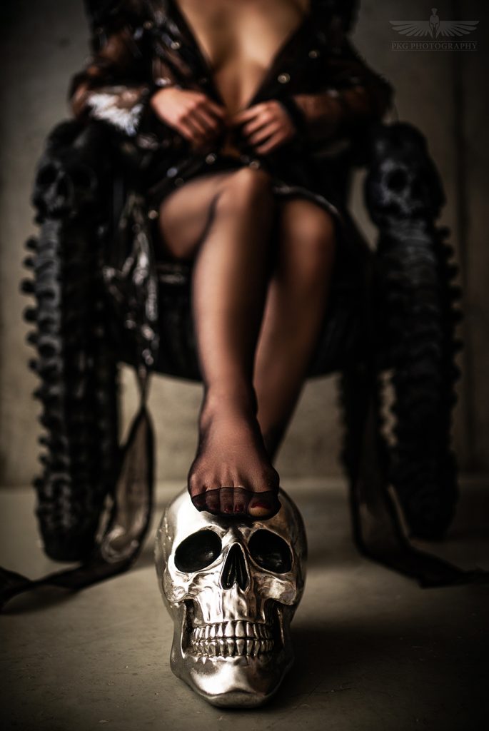 Lady Amanita sitzend, den Fuß auf einem silbernen Totenkopf